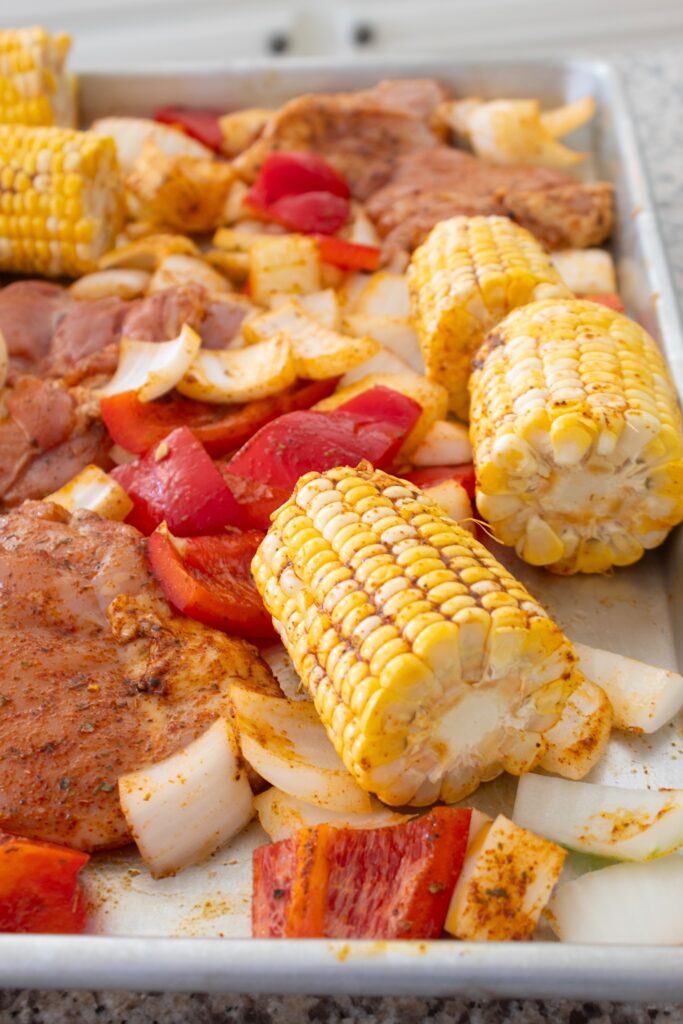 chicken before baking on a sheet pan with corn and onions with bell peppers
