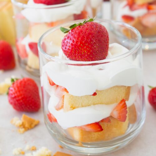 layered strawberry shortcake cup with whipped cream, cake and strawberries in a clear glass