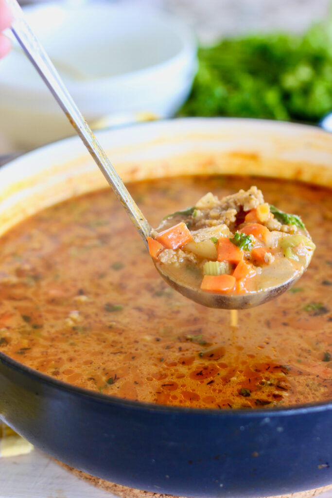 a ladel of soup in a blue bowl with potatoe and sausage soup